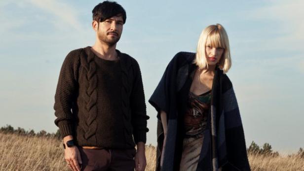 Ein Mann mit Zopfmusterpullover und eine Frau mit Poncho stehen auf einem Feld.