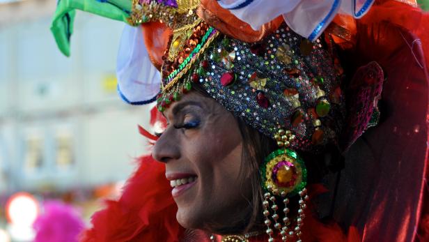 Eine lächelnde Person mit einem aufwendigen, farbenfrohen Kopfschmuck.