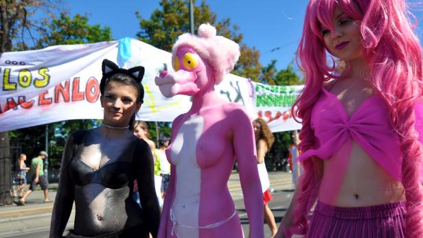 Drei Personen in Kostümen nehmen an einer Parade oder Demonstration im Freien teil.