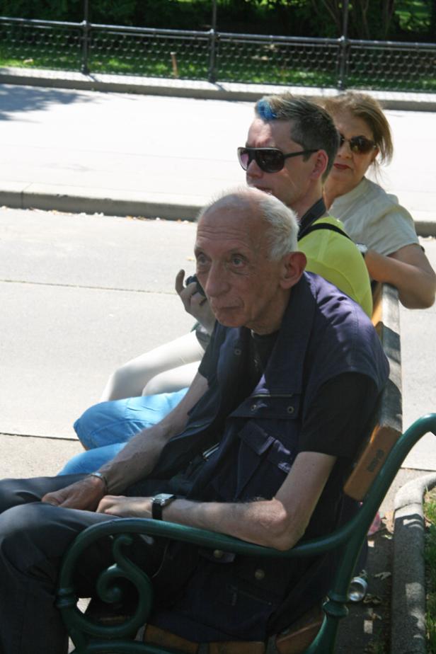 Drei Personen sitzen auf einer Parkbank im Freien.