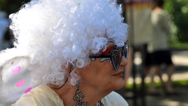 Eine Person mit weißer Perücke und herzförmiger Sonnenbrille im Profil.