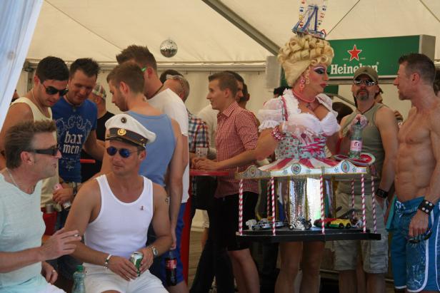 Eine Dragqueen mit einem Karussell-Kostüm steht inmitten einer Menschenmenge.