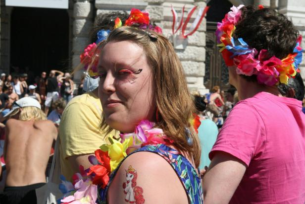 Eine Frau mit Blumenkranz und Einhorn-Tattoo auf der Schulter feiert auf einer Parade.