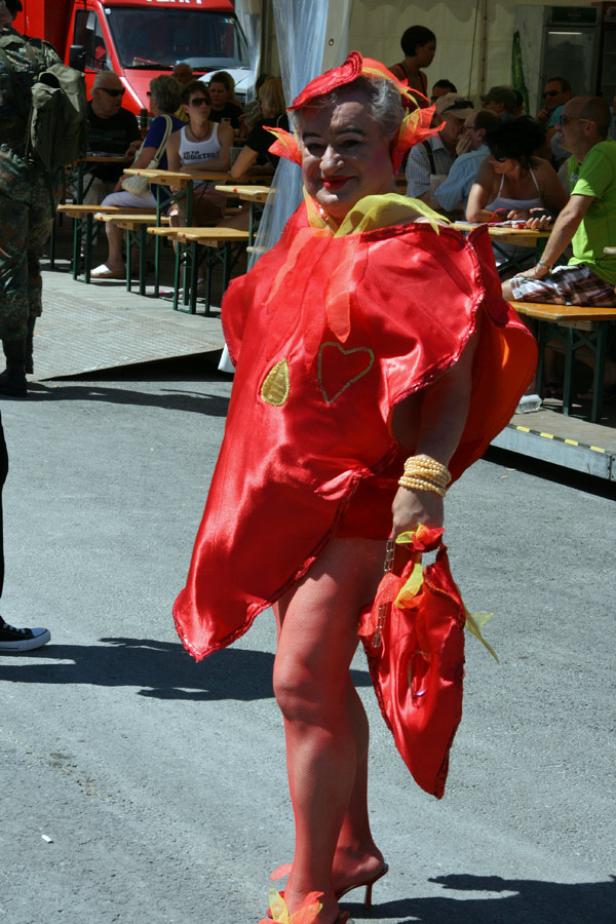 Eine Person in einem roten Blumenkostüm mit passenden Accessoires steht auf der Straße.