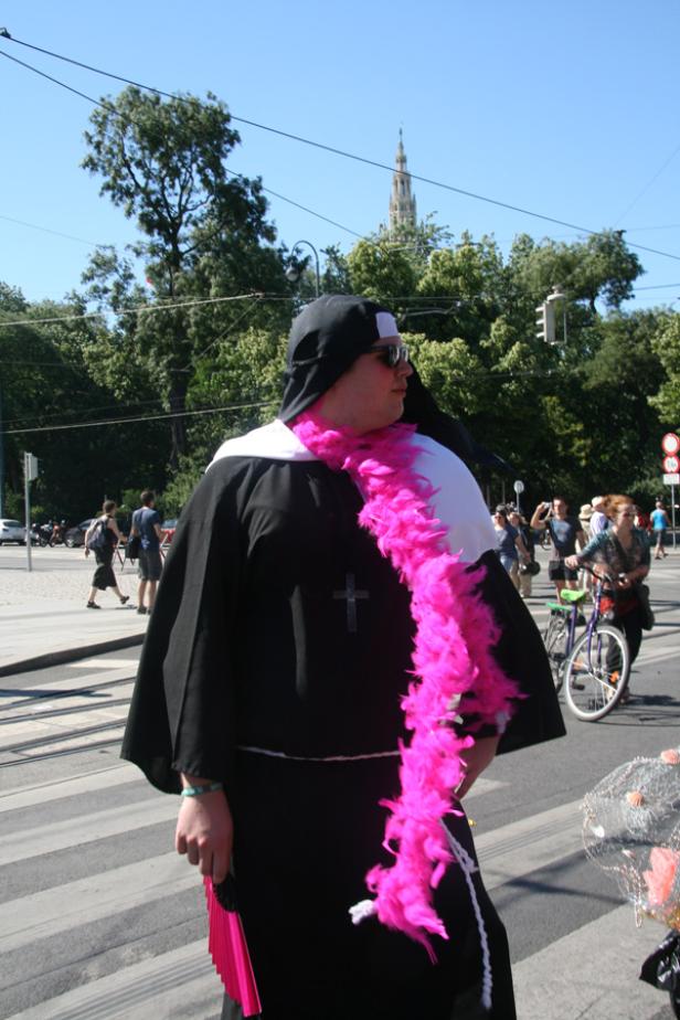 Eine als Nonne verkleidete Person mit pinkfarbener Federboa auf einer Straße.