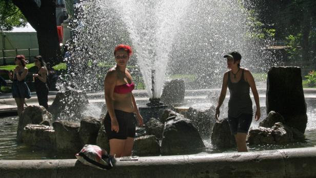 Mehrere Personen stehen in einem Brunnen und erfrischen sich an einem sonnigen Tag.