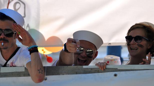 Drei Personen in Matrosenuniformen feiern, eine raucht, eine zeigt auf die Kamera.