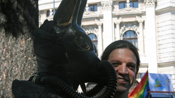 Eine Person mit einer Anubis-Maske und einem Atemgerät steht vor einem Gebäude.