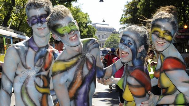 Vier Menschen mit Körperbemalung stehen lächelnd auf einer Straße.