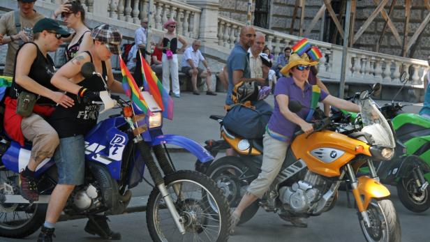Zwei Frauen auf Motorrädern mit Regenbogenflaggen nehmen an einer Parade teil.