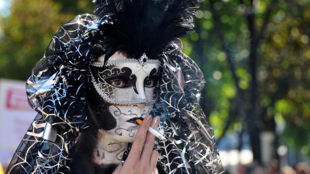 Eine Person mit aufwendiger Maske und Kostüm raucht eine Zigarette.