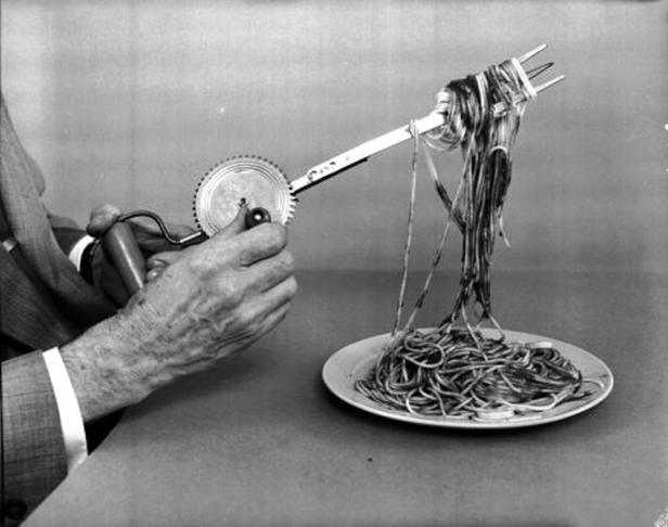 Eine Person benutzt einen Handmixer, um Spaghetti auf eine Gabel zu wickeln.