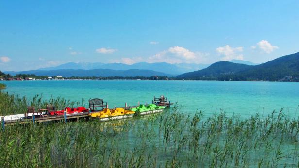 Ein Steg mit Tretbooten führt in einen türkisfarbenen See vor einer Bergkulisse.