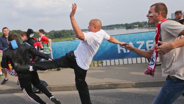 Ein Mann tritt einen anderen Mann vor dem Hintergrund einer Menschenmenge und eines Flusses.