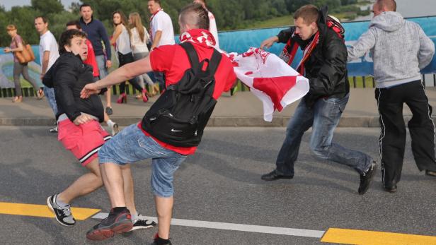 Mehrere Personen scheinen sich auf einer Straße zu schubsen, einige schwenken polnische Flaggen.