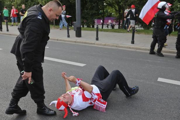 Ein Polizist steht neben einem am Boden liegenden Mann in polnischer Fankleidung.