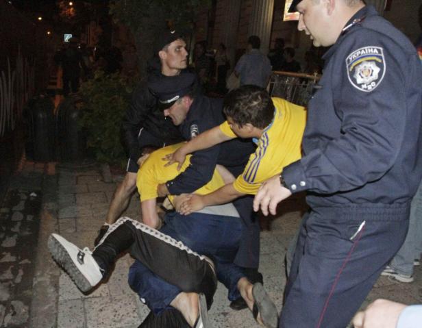 Polizisten nehmen eine Person in einem gelben Trikot fest.