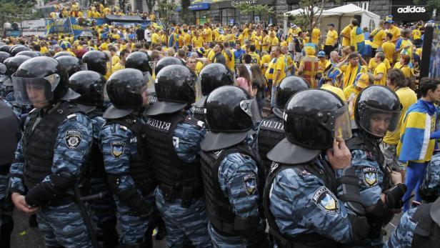 Eine Reihe von Polizisten in Kampfmontur steht vor einer Menschenmenge in gelben T-Shirts.