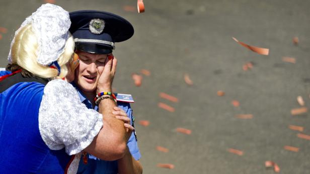 Ein Polizist wird von einer Person in Tracht und Perücke umarmt, während Konfetti fällt.