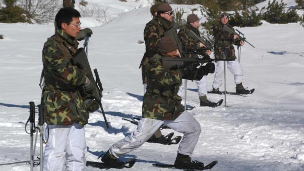 Soldaten in Winterkleidung und Schneeschuhen zielen mit Gewehren im Schnee.