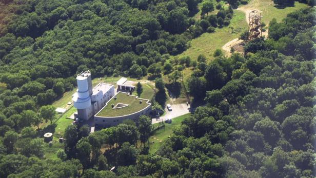 Luftaufnahme eines Observatoriums inmitten eines dichten Waldes mit einem hölzernen Aussichtsturm in der Nähe.