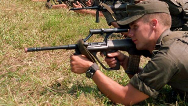 Ein Soldat liegt im Gras und zielt mit einem Gewehr.