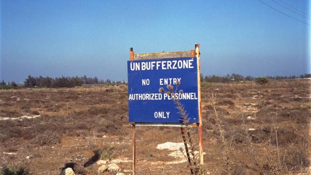 Ein blaues Schild mit der Aufschrift „UN Bufferzone. No Entry. Authorized Personnel Only“ in einem trockenen Feld.