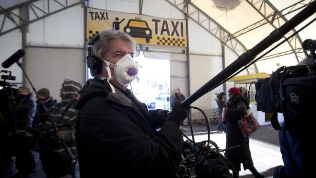 Ein Tontechniker mit Maske und Kopfhörern bei Dreharbeiten im Taxi-Gewerbe.