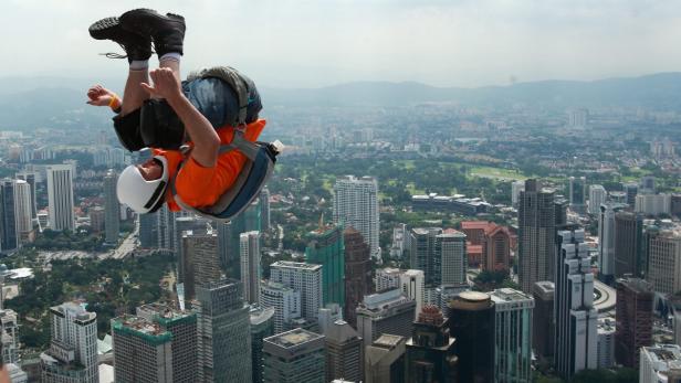Ein Basejumper stürzt sich vor der Skyline einer Großstadt in die Tiefe.