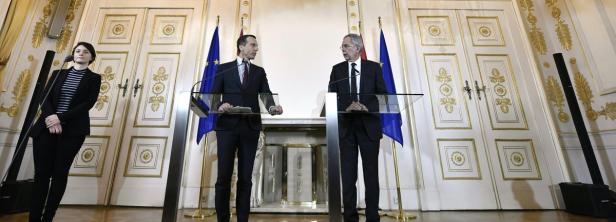 Zwei Männer stehen an Rednerpulten vor Flaggen und einer Frau in einem eleganten Raum.