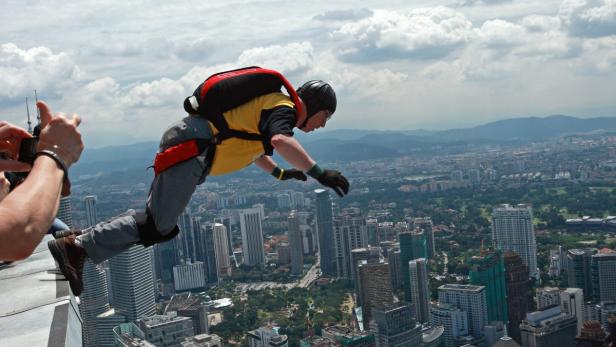 Ein Mann springt mit einem Fallschirm von einem hohen Gebäude in eine Stadt.