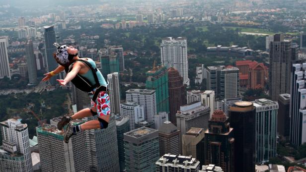 Eine Frau springt mit einem Fallschirm von einem Hochhaus in einer Stadt.