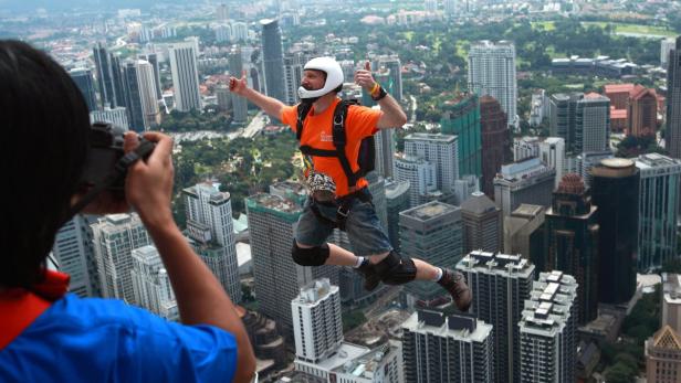 Ein Mann springt mit Helm und Sicherheitsausrüstung von einem Hochhaus in Kuala Lumpur.