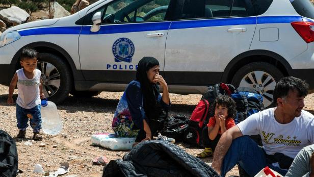 Eine Familie sitzt erschöpft vor einem griechischen Polizeiauto.
