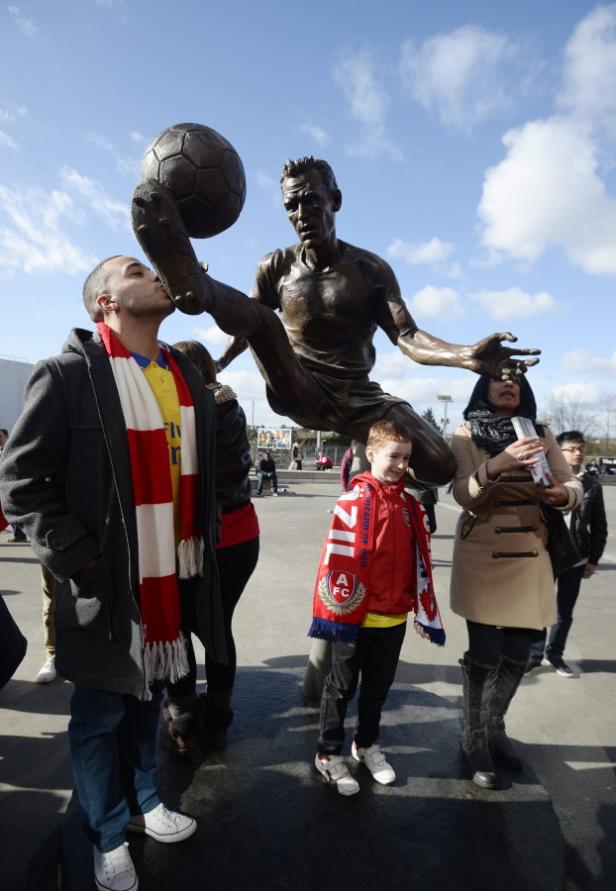 BRITAIN SOCCER ENGLISH PREMIER LEAGUE Menschen posieren vor einer Statue eines Fußballspielers mit einem Ball am Fuß.