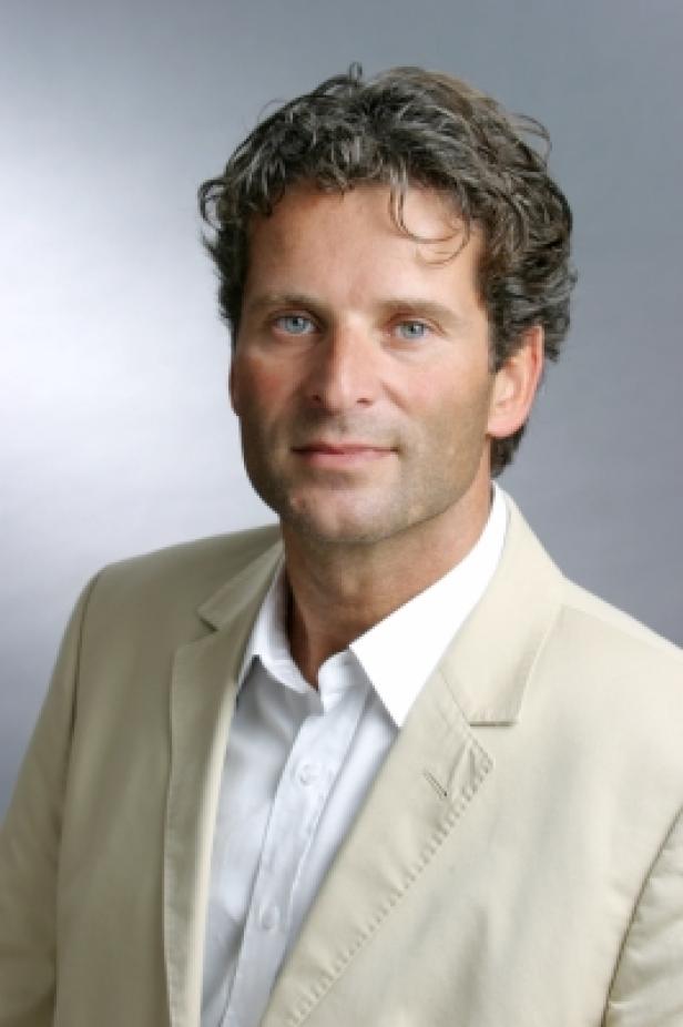 Ein Mann mit braunen Haaren und einem hellen Sakko blickt in die Kamera.