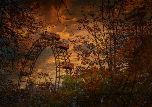 Das Wiener Riesenrad im goldenen Abendlicht, gesehen durch herbstliche Bäume.