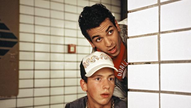 Zwei junge Männer stehen hinter einer Ecke in einem Raum mit weißen Fliesen.