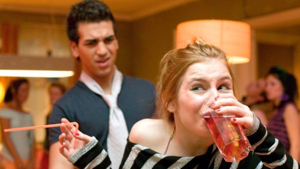 Eine junge Frau trinkt auf einer Party einen rosafarbenen Cocktail.