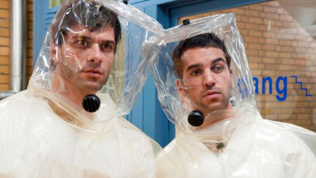 Zwei Männer tragen Schutzanzüge mit transparenten Hauben.