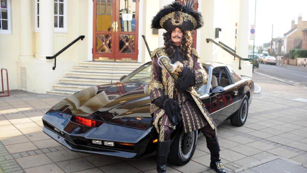 Ein Mann im Piratenkostüm posiert vor einem schwarzen Auto.