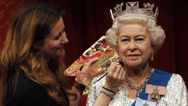 Eine Frau retuschiert die Wachsfigur von Königin Elisabeth II. mit einem Pinsel.