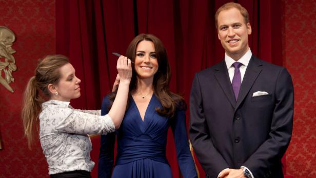 Eine Frau korrigiert das Make-up der Wachsfigur von Kate Middleton, während Prinz William daneben steht.
