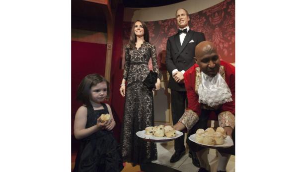 Eine junge Besucherin isst einen Scone neben den Wachsfiguren von Prinz William und Prinzessin Kate.