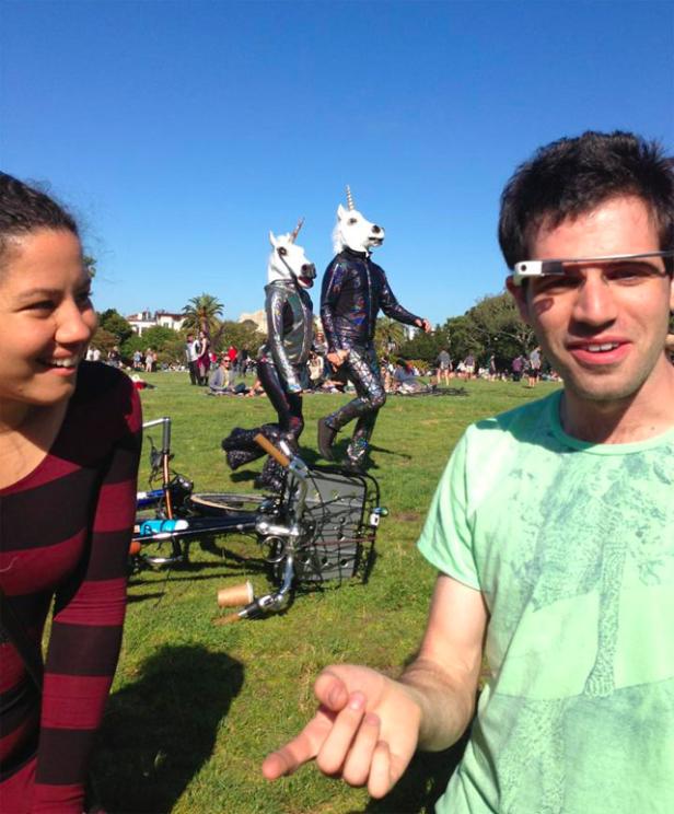 Zwei Personen in Einhornkostümen stehen auf einer Wiese, während ein Mann Google Glass trägt.