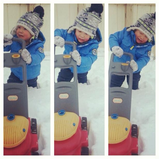 Ein kleiner Junge schiebt einen Spielzeug-Rasenmäher durch den Schnee.