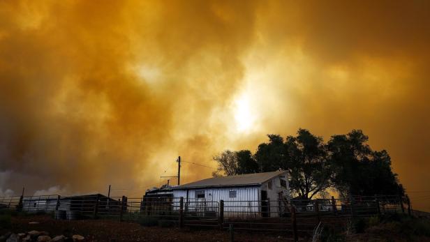 Ein kleines, weißes Haus unter einem orangefarbenen Himmel, vermutlich durch Rauch von einem Waldbrand verursacht.
