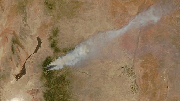 Satellitenansicht eines Waldbrandes, der Rauchwolken über eine trockene Landschaft schickt.