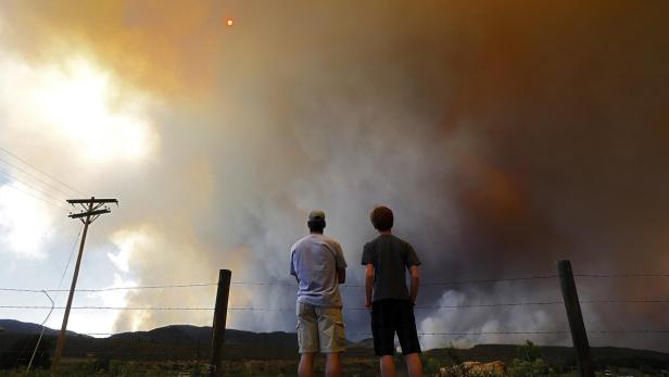 Zwei Personen beobachten einen Waldbrand am Horizont.