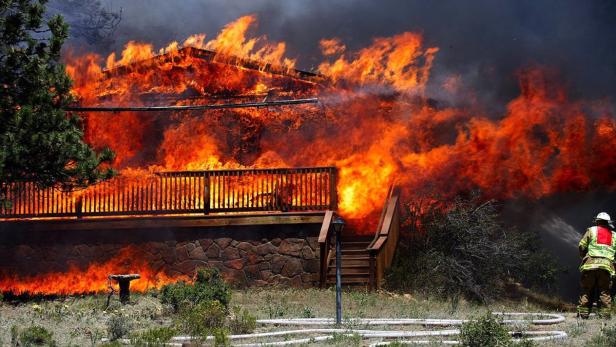 Ein Haus steht in Flammen, während ein Feuerwehrmann versucht, das Feuer zu löschen.